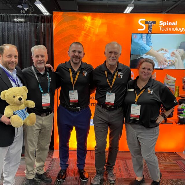 A group of employees standing in front of an orange backdrop at a trade show.